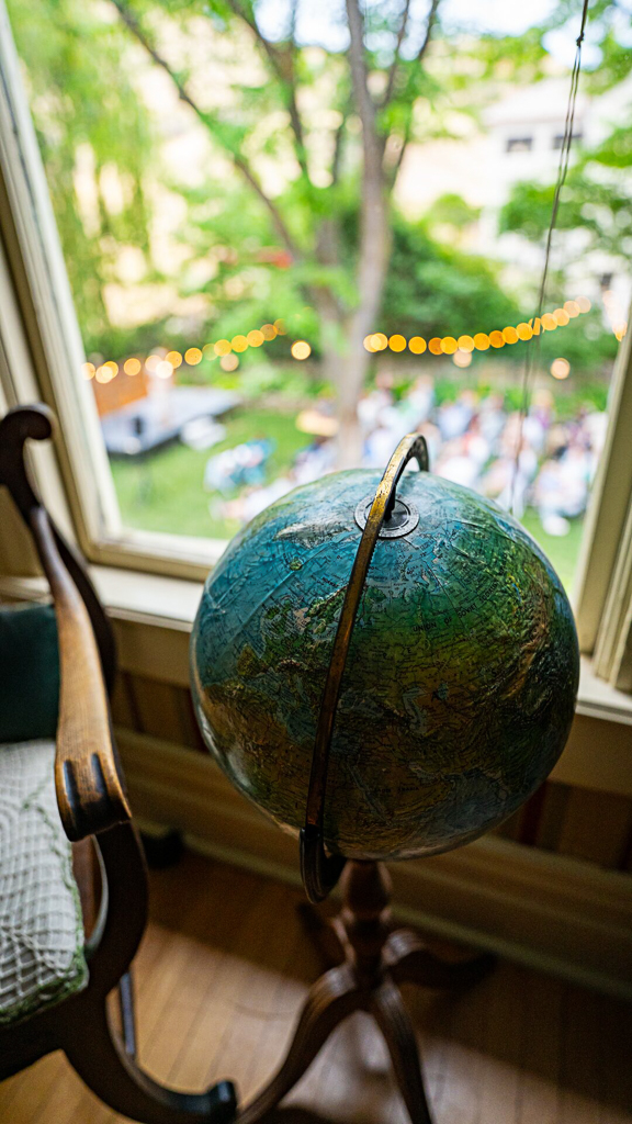 Vintage globe beside an interior window with warm string lights glowing over a garden event outside