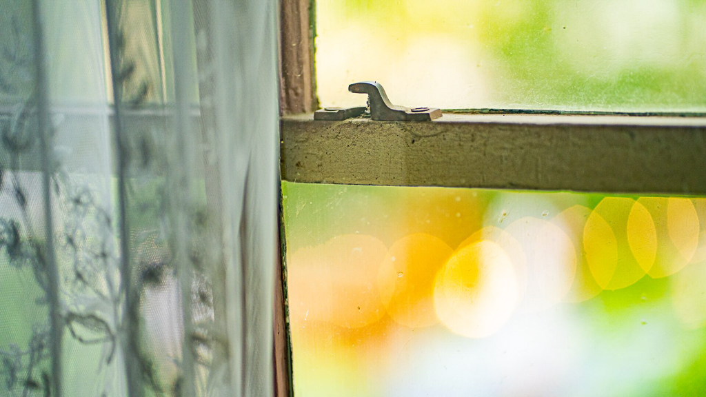 Close-up of a vintage window latch with lace curtain and soft bokeh from garden lights outside