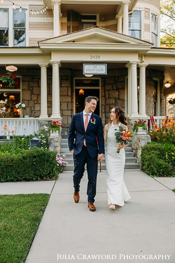 Bride and groom walking hand in hand in front of the house