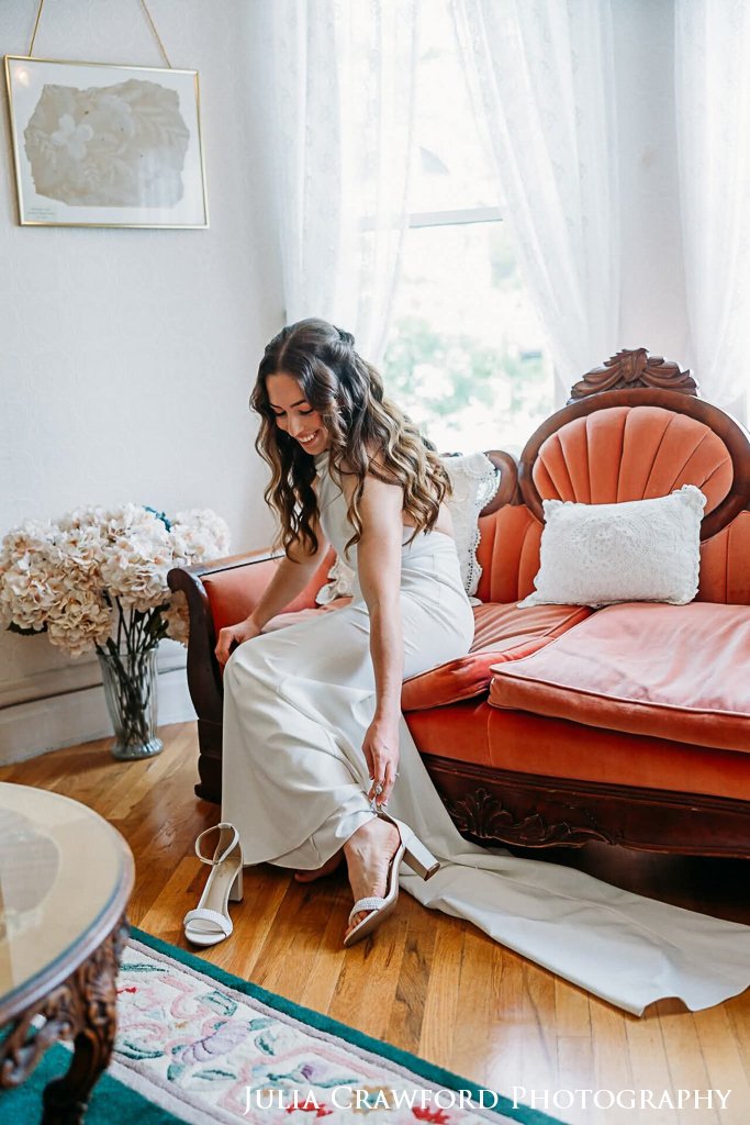 Bride putting on her shoes on an antique settee before the ceremony