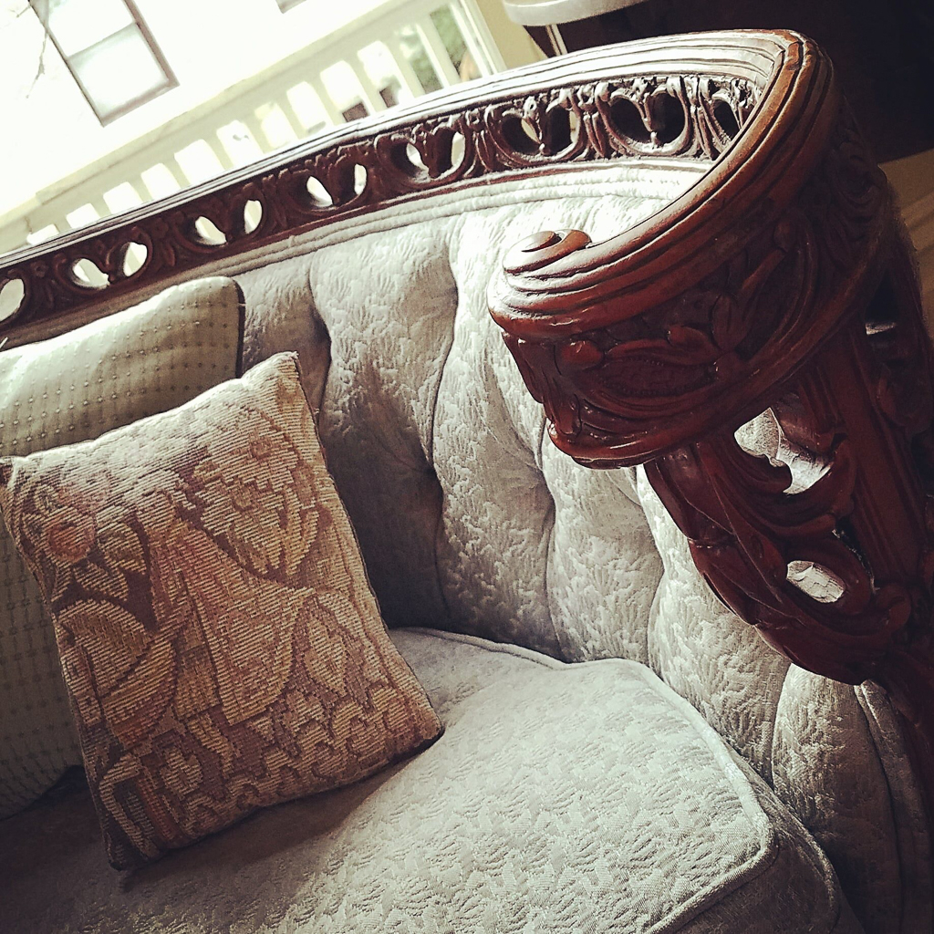 Close-up of an ornately carved Victorian settee with cream brocade upholstery and a tapestry throw pillow